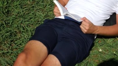 Yakışıklı adam parkta bir ağacın altında çimlerin üzerine oturmuş kitap, 4 k, yavaş hareket okuma