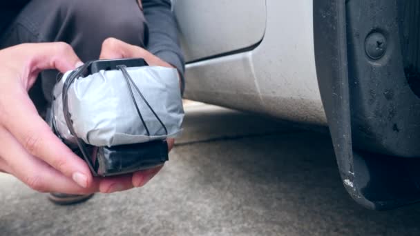 Un hombre pone un artefacto explosivo casero debajo del auto. Preparación del acto terrorista. 4k. Movimiento lento — Vídeos de Stock