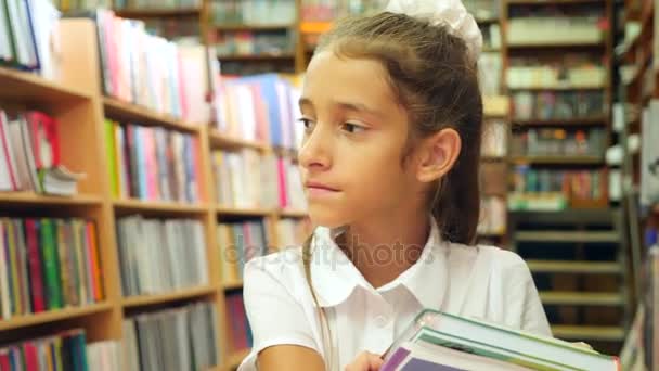 Портрет девочки 8 - 12 лет, стоящей в библиотеке. Книжные полки на заднем плане. 4k, slow motion — стоковое видео