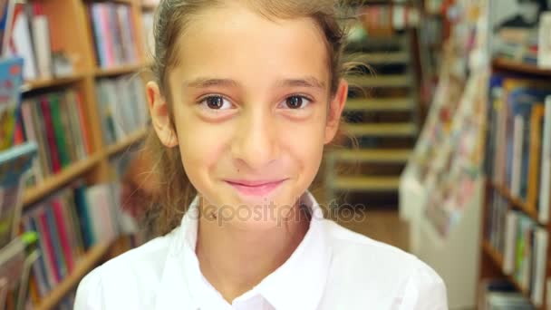 Portrait of a girl 8 - 12 years old, standing in the library. Bookshelves of a bookcase in the background. 4k, slow motion