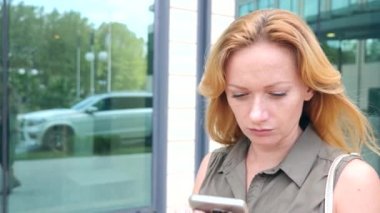 Kız telefon ile. sıcak güneşli bir günde modern bir şehir içinde yürür. gökdelenlerin arka plan. 4 k. ağır çekim.