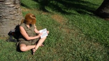 sarışın kadın parkta çim bir ağacın altında oturup kitap okuma. 4k, ağır çekim