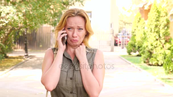 La femme se sent triste et pleure, parlant à quelqu'un sur le téléphone portable. est dans le parc d'été. 4k. Mouvement lent — Video