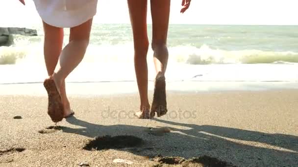 Madre e hija caminan en la orilla del mar, salpicaduras de agua en sus pies, movimientos lentos. La ola cierra las piernas de los que caminan. 4k — Vídeos de Stock