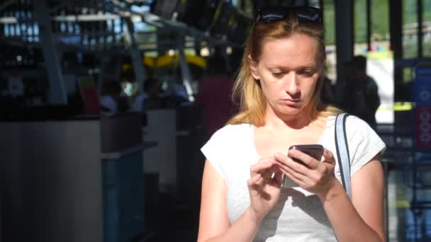 Kvinnan använder en smartphone i flygplats väntar lounge. Förväntningar på flyg på flygplatsen. 4k, Slowmotion — Stockvideo