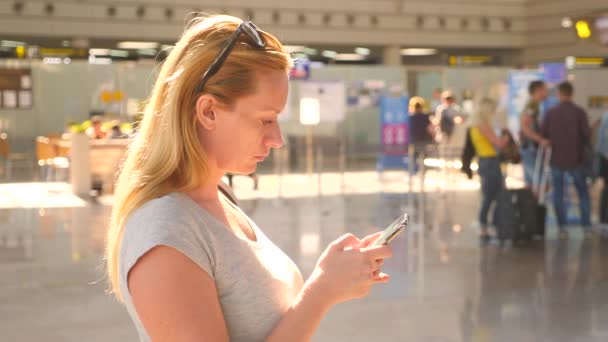 Женщина пользуется смартфоном в зале ожидания аэропорта. Ожидания полета в аэропорту. 4k, slow motion — стоковое видео