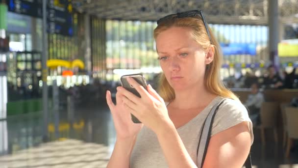 Frau benutzt Smartphone in Flughafen-Wartehalle. Flugerwartungen am Flughafen. 4k, Zeitlupe — Stockvideo