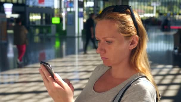 Mulher usa um smartphone na sala de espera do aeroporto. Expectativas de voo no aeroporto. 4k, câmera lenta — Vídeo de Stock