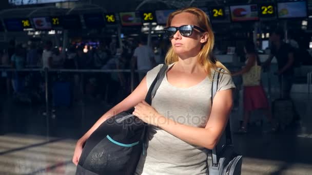 Mujer en la sala de espera del aeropuerto. Expectativas de vuelo en el aeropuerto. 4k, cámara lenta, la chica en el aeropuerto mira el tablero de información . — Vídeos de Stock