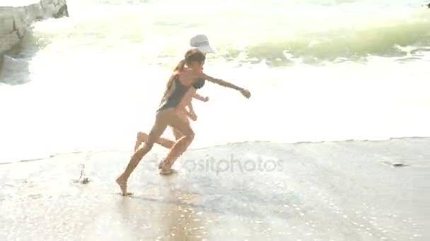 Mor och dotter promenad på stranden, vattenstänk på fötter, långsamma rörelser. Vågen stänger benen på dem, som vandrar. 4k — Stockvideo
