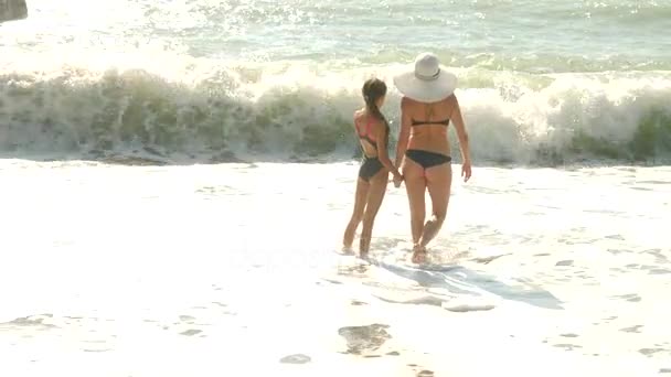 Mother and daughter walk on the seashore, splashes of water on their feet, slow movements. The wave closes the legs of those who walk. 4k — Stock Video