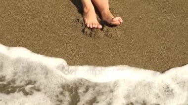 Ağır çekim yakın çekim: Genç kadın, kumsalda yürüyüş ve deniz suyu kameraya püskürtme uzun bacakları var. 4k