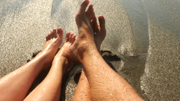 O casal está sentado na praia. Close Up Of Feet And Waves. Movimento lento. 4k — Vídeo de Stock