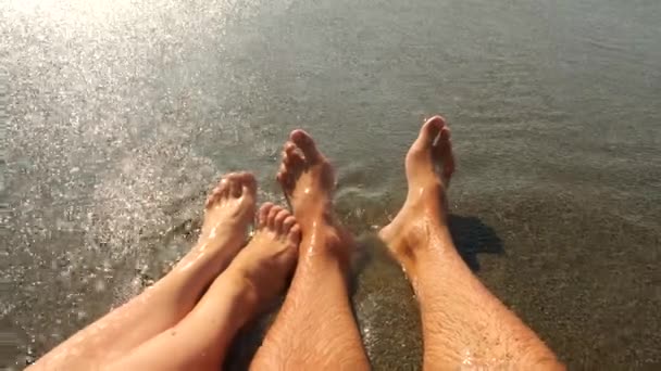 O casal está sentado na praia. Close Up Of Feet And Waves. Movimento lento. 4k — Vídeo de Stock