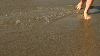 Ağır çekim yakın çekim: Genç kadın, kumsalda yürüyüş ve deniz suyu kameraya püskürtme uzun bacakları var. 4k