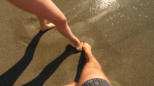 Pareja de amantes hombre y mujer pintan con los pies en el corazón de arena mojada. El corazón es lavado por una ola. pareja en la costa del mar. 4k, cámara lenta — Vídeo de stock