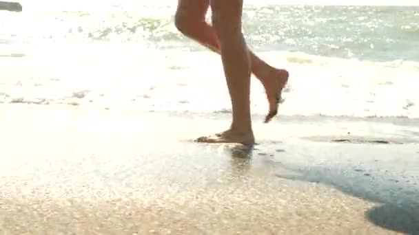 Ağır çekim yakın çekim: Genç kadın, kumsalda yürüyüş ve deniz suyu kameraya püskürtme uzun bacakları var. 4k — Stok video