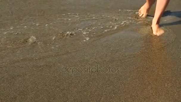Медленное приближение: молодая женщина с длинными ногами, идущая по пляжу и брызгающая морской водой в камеру. 4k — стоковое видео