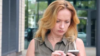 Kız telefon ile. sıcak güneşli bir günde modern bir şehir içinde yürür. gökdelenlerin arka plan. 4 k. ağır çekim.
