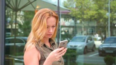 Kız telefon ile. sıcak güneşli bir günde modern bir şehir içinde yürür. gökdelenlerin arka plan. 4 k. ağır çekim.