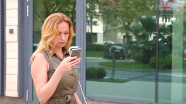 Kız telefon ile. sıcak güneşli bir günde modern bir şehir içinde yürür. gökdelenlerin arka plan. 4 k. ağır çekim.