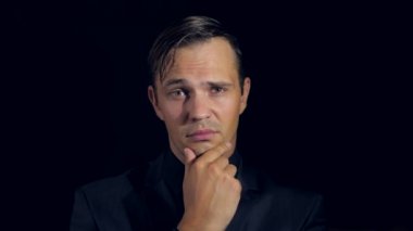 portre siyah arka plan üzerine siyah giysili bir adam. 4 k. ağır çekim. adam çenesini konturlar ve kameraya benziyor. karar verme jest