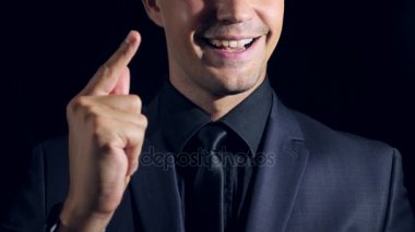 siyah bir arka plan üzerinde siyah giysili bir adam süper yakın çekim. 4 k. ağır çekim. adamın parmaklarını tıklatır ve bir fikir jest, onun parmağı yükseltir