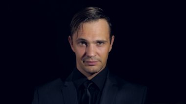 portre siyah arka plan üzerine siyah giysili bir adam. 4 k. ağır çekim. adam kendine gülümser parmağını çağırıyor ve kameraya doğru görünüyor