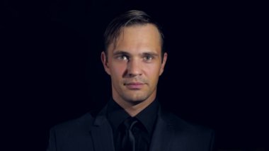 portre siyah arka plan üzerine siyah giysili bir adam. 4 k. ağır çekim. adam kendine gülümser parmağını çağırıyor ve kameraya doğru görünüyor