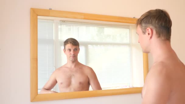 Un mec mignon gai s'habille devant un miroir et sourit à son reflet. 4k, au ralenti. répète un sourire — Video