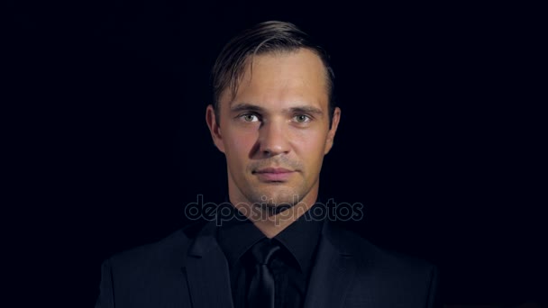 Closeup of a man in black clothes on black background. 4k. Slow motion. man beckons his finger to himself, smiles and looks into the camera — Stock Video