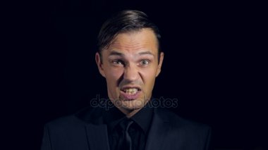 portre siyah arka plan üzerine siyah giysili bir adam. 4 k. ağır çekim. adam indignantly silkiyor ve eliyle yüzünü kapatır.