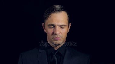 portre siyah arka plan üzerine siyah giysili bir adam. 4 k. ağır çekim. adam indignantly silkiyor ve eliyle yüzünü kapatır.