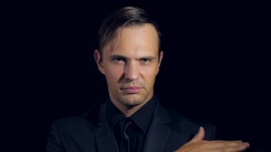 portre siyah arka plan üzerine siyah giysili bir adam. 4 k. ağır çekim. baştan çıkarıcı kameraya bakarak ve gülümseyen bir adamdır