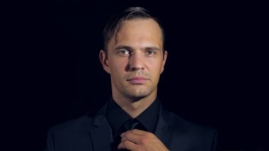 portre siyah arka plan üzerine siyah giysili bir adam. 4 k. ağır çekim. adam kravatını gülümsüyor ayarlar ve kameraya doğru görünüyor