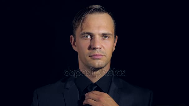 Closeup of a man in black clothes on black background. 4k. Slow motion. man adjusts his tie, smiles and looks into the camera — Stock Video