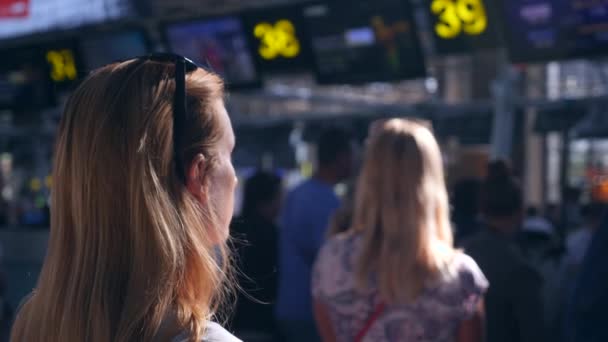 Frau in der Wartehalle des Flughafens. Flugerwartungen am Flughafen. 4k, Zeitlupe, das Mädchen am Flughafen blickt auf die Informationstafel. — Stockvideo