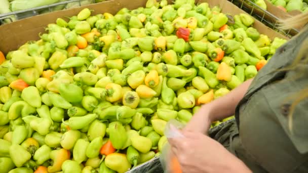 Uma mulher em um supermercado em uma prateleira de vegetais, compra legumes e frutas. O homem escolhe pimenta búlgara. Movimento lento, 4k — Vídeo de Stock