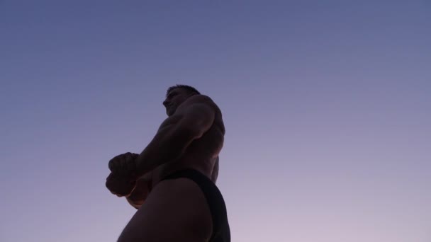 Silhueta de um fisiculturista masculino. belo atleta posando na praia ao pôr do sol. 4K. tiro lento — Vídeo de Stock