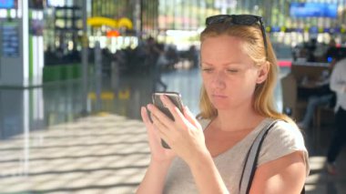 Kadın bir smartphone Havaalanı lounge bekleyen kullanır. Havaalanında uçuş beklentilerini. 4k, ağır çekim