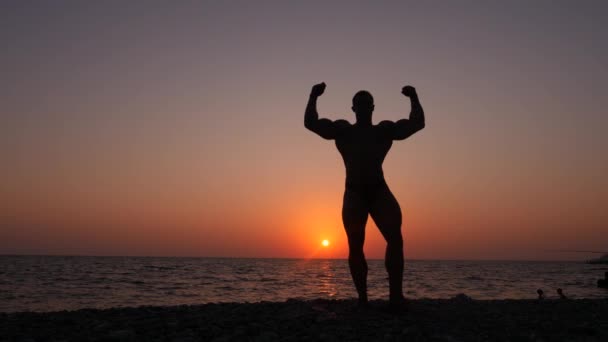 男性健美的轮廓。美丽的运动员在日落时分在沙滩上合影。4 k.缓慢射击 — 图库视频影像