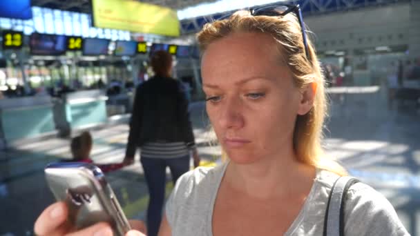Frau benutzt Smartphone in Flughafen-Wartehalle. Flugerwartungen am Flughafen. 4k, Zeitlupe — Stockvideo