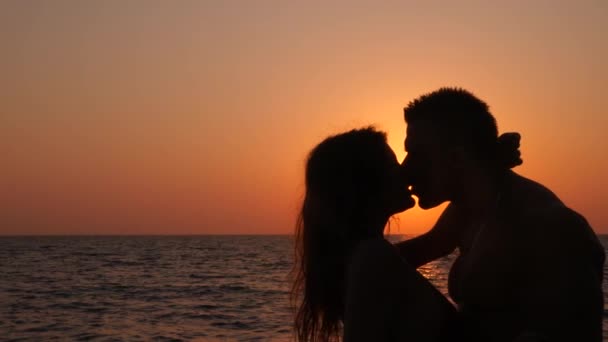 Silhouettes of pregnant women in bikini and romantic muscular man. the bodybuilder hugs, kisses his wife and strokes her belly. against the background of a sea sunset. 4k. Slow motion — Stock Video