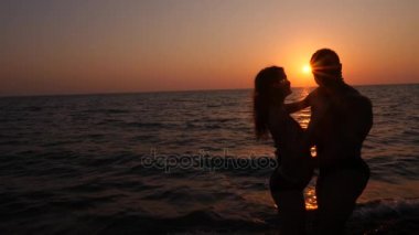 Bikini ve romantik kaslı adam hamile kadın siluetleri. vücut geliştirmeci hugs, karısını öpüyor ve karnı vuruş. Deniz günbatımı arka planı. 4 k. ağır çekim