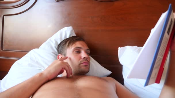 Muž, čtení knihy, ležící v posteli doma. 4 k Zpomalený pohyb — Stock video