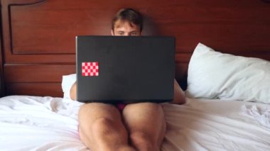 Parlak yatak odasında yatakta çalışan mutlu yakışıklı adam. 4k, ağır çekim