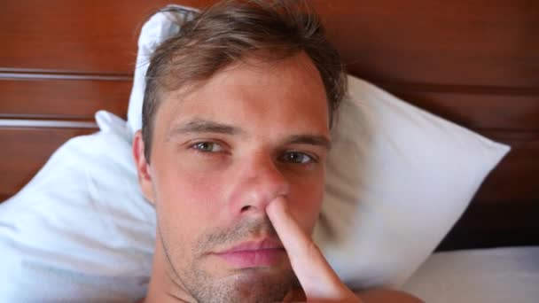 Портрет молодого человека с глупой гримасой, лежащего на кровати. 4k slow motion — стоковое видео