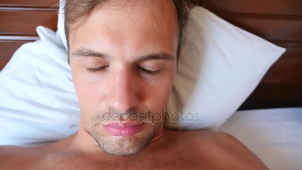Portrét mladého muže s hloupé grimasy, ležící na posteli. 4 k Zpomalený pohyb — Stock video