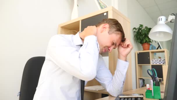 Молодой человек страдает от боли в шее во время работы за компьютером. 4k, slow motion — стоковое видео