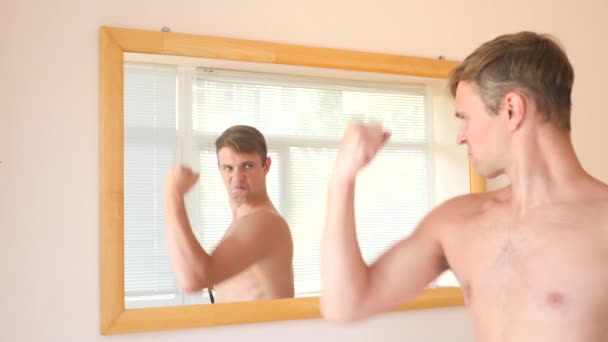 El alegre chico agradable se desnuda frente al espejo y sonríe ante su reflejo. 4k, cámara lenta — Vídeo de stock